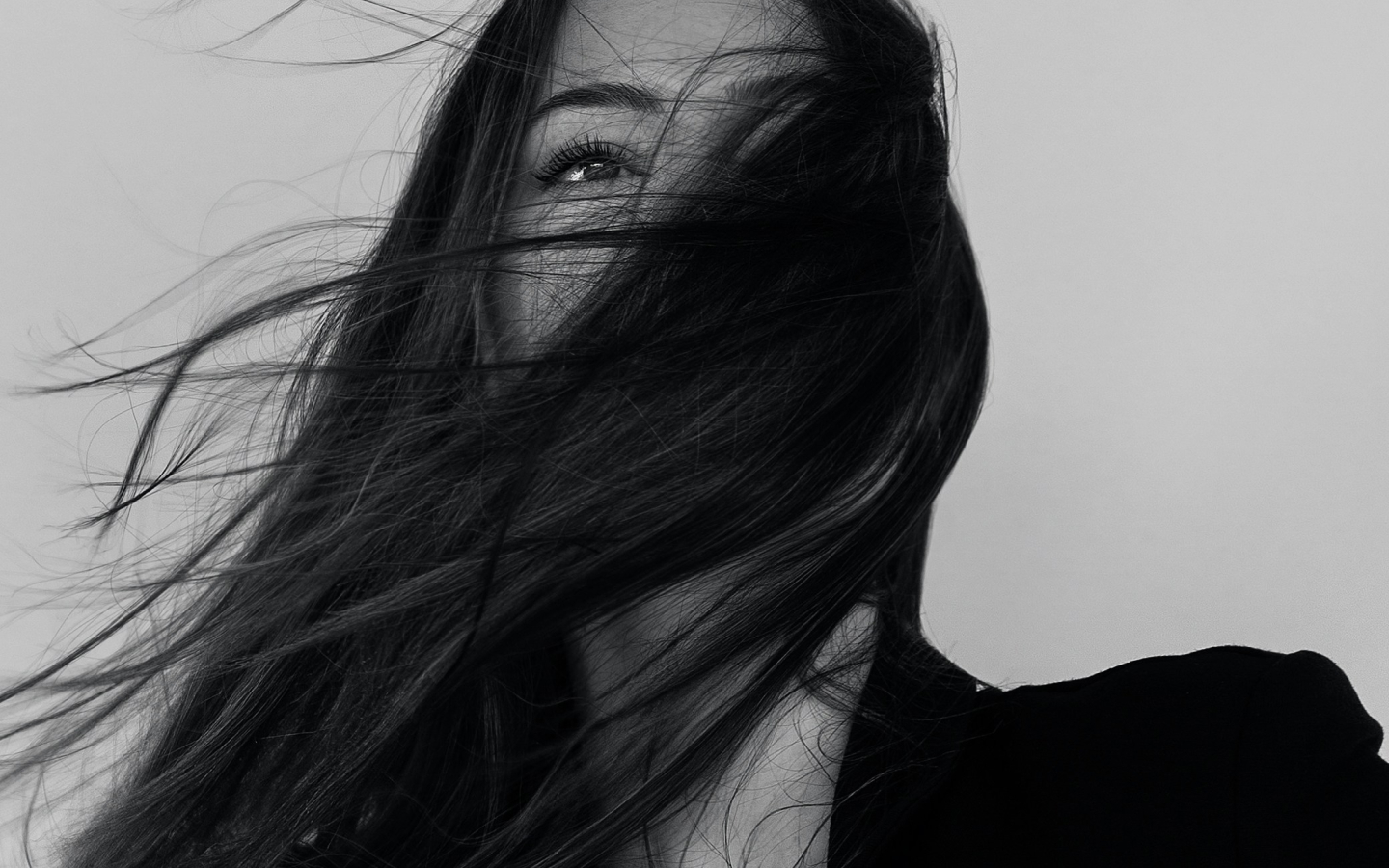 A black-and-white close-up portrait of a woman with her face partially obscured by her flowing dark hair creates a mysterious and artistic effect.